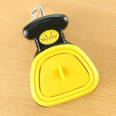 Yellow foldable dog pooper scooper closed on a wooden table, with carabiner clip on the handle