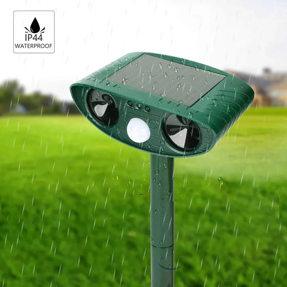 Green solar ultrasonic repellent staked in a grassy yard during rainfall, covered in water droplets, with an IP44 waterproof badge in the corner.