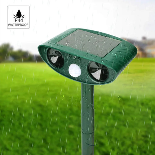 Green solar ultrasonic repellent staked in a grassy yard during rainfall, covered in water droplets, with an IP44 waterproof badge in the corner.