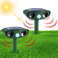Pair of green solar ultrasonic repellents planted in a bright grassy lawn under the sun, broadcasting red ultrasonic waves across the yard.