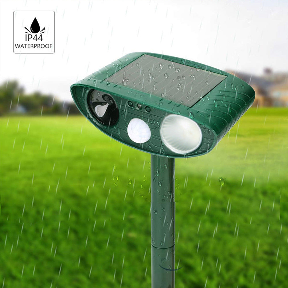 Green solar repellent on a stake out in the rain with a bright LED flash lit, water beading on its surface, and an IP44 waterproof badge in the corner.