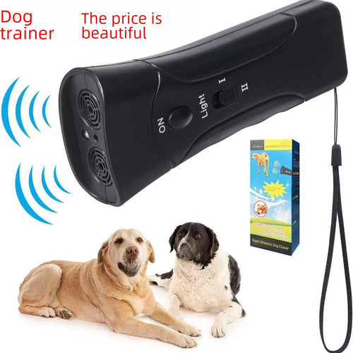 Handheld black ultrasonic dog trainer emitting sound waves above its retail box and wrist strap, with a Labrador and a black-and-white dog resting below.