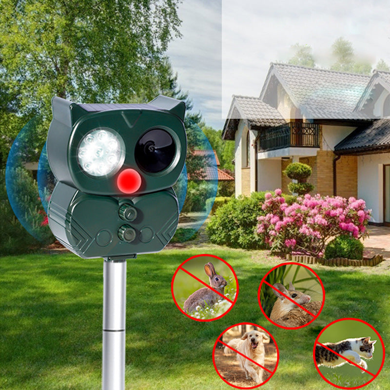 Owl-shaped solar repellent with lit LEDs and red sensor on a stake in front of a house and garden, emitting blue waves above crossed-out rabbit, squirrel, dog, and cat icons.
