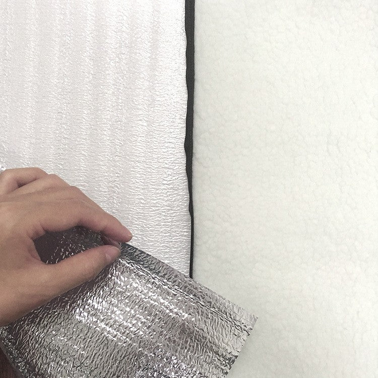 Hand lifting the silver reflective thermal layer of the dog kennel mat to reveal the white fleece interior insulation