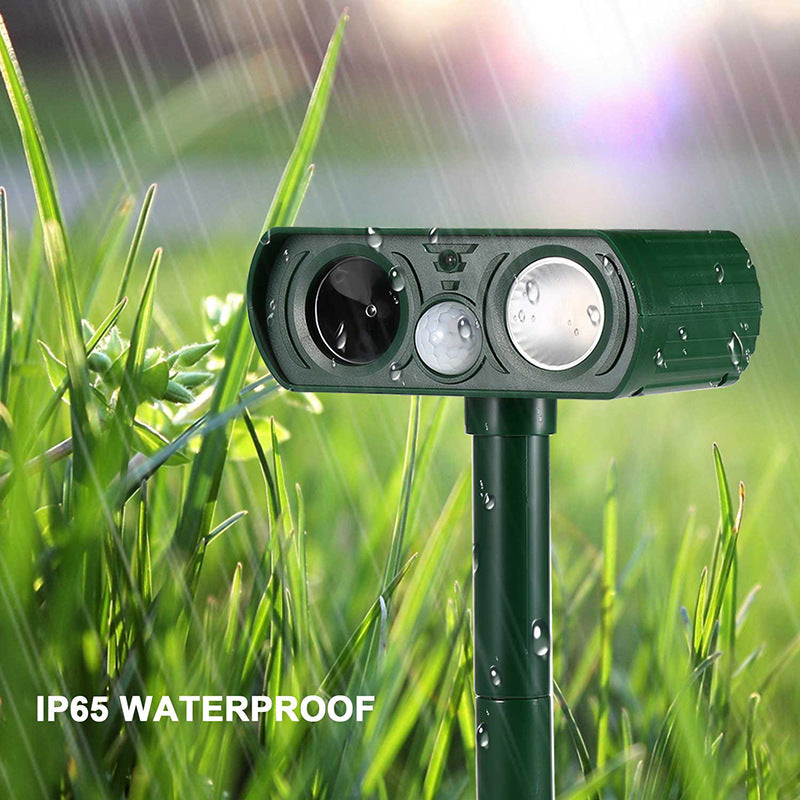 Green solar repellent staked among tall grass in the rain with its LED light glowing and water droplets on it, captioned IP65 waterproof.