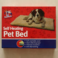 Front of the Pet Comforts self-heating dog bed retail box featuring a spaniel lying on the tan mat and a feature list for the thermal insulating cover